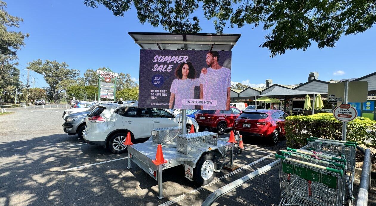 Mobile billboard trailer with a digital LED advertising screen displaying a retail promotion in a busy Melbourne shopping centre car park.